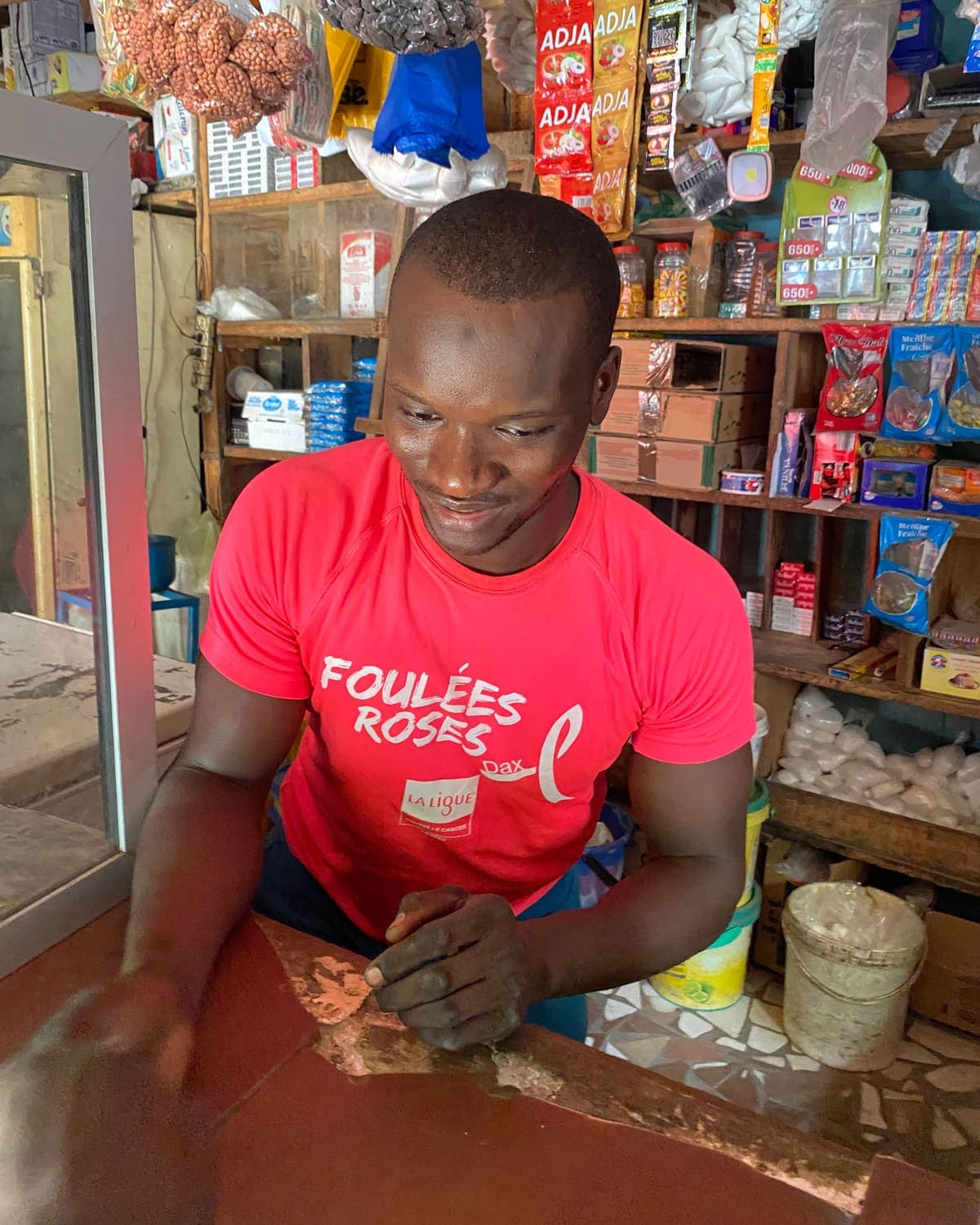 Un commerçant sourit derrière le comptoir de sa boutique de quartier, rayons pleins derrière lui